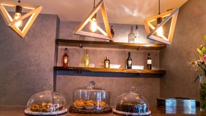 Zona de bar amb prestatges de fusta que mostren ampolles, taulell de marbre amb aliments i llums penjants.