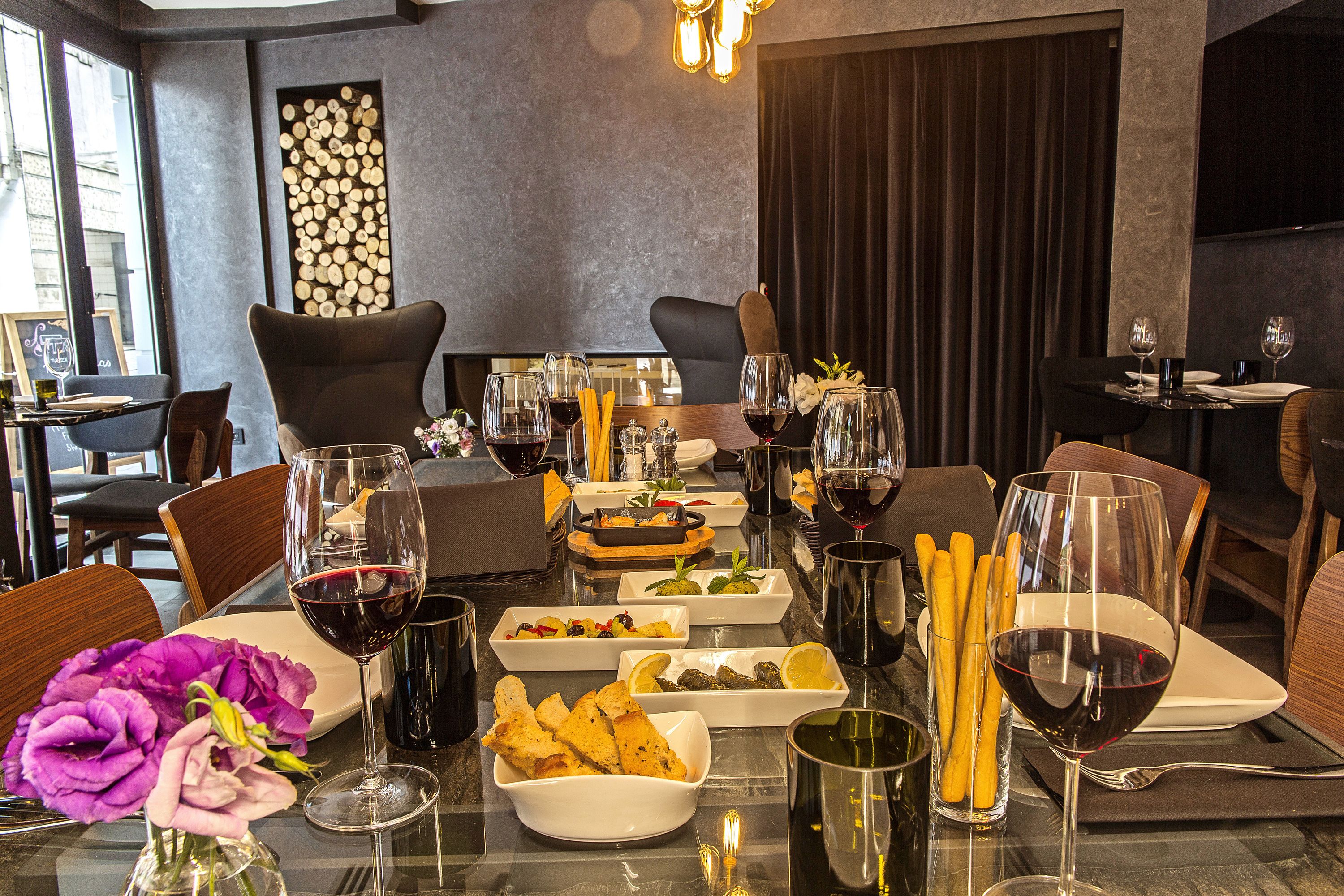 A dining table set with various dishes, glasses of red wine, and a vase of purple flowers.