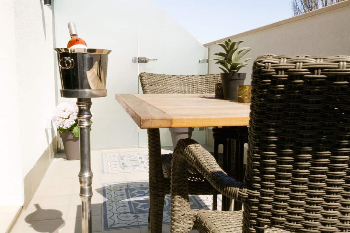 A wicker chair, a wooden table, and a potted plant in an outdoor seating area.