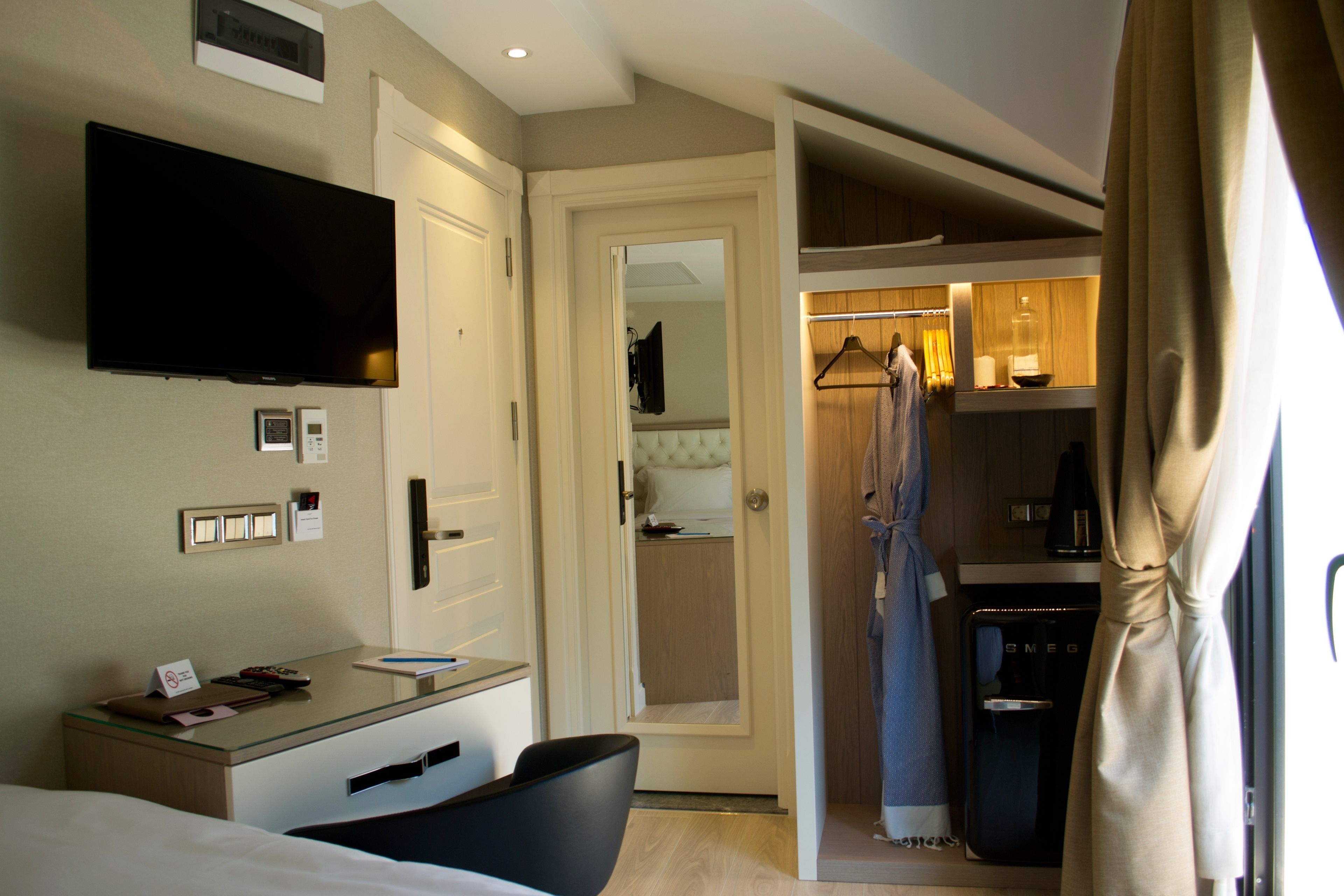 A hotel room with a bed, a desk with a flat-screen TV, a coat rack, and a wardrobe.