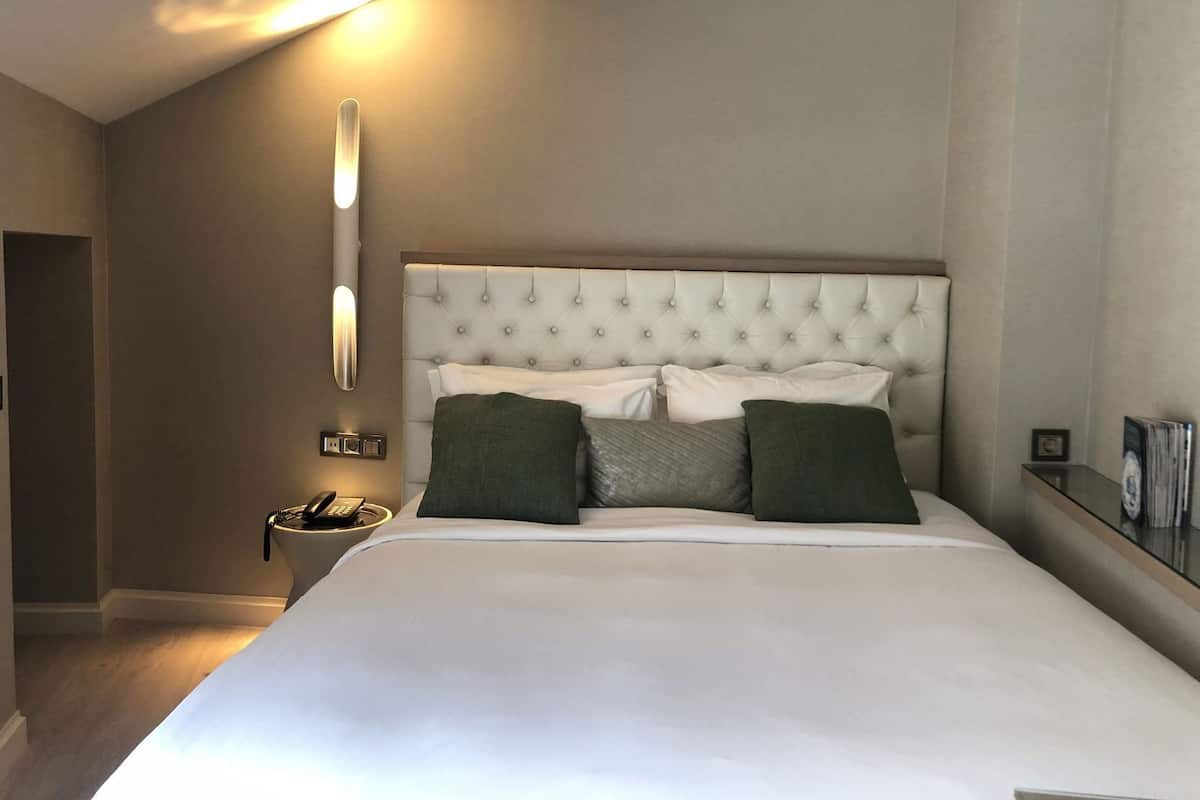A hotel room with a large bed, a bedside table with a lamp, and a wall-mounted light fixture.