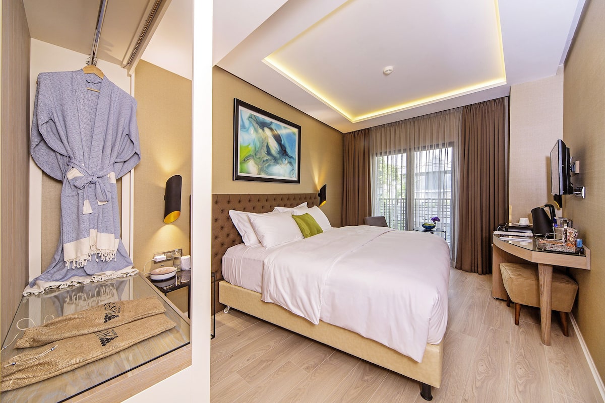 A hotel room with a large bed, a desk, a chair, a TV, and a painting on the wall.