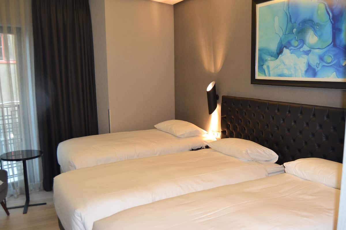 A hotel room with two beds, a small table, a chair, and a painting on the wall.