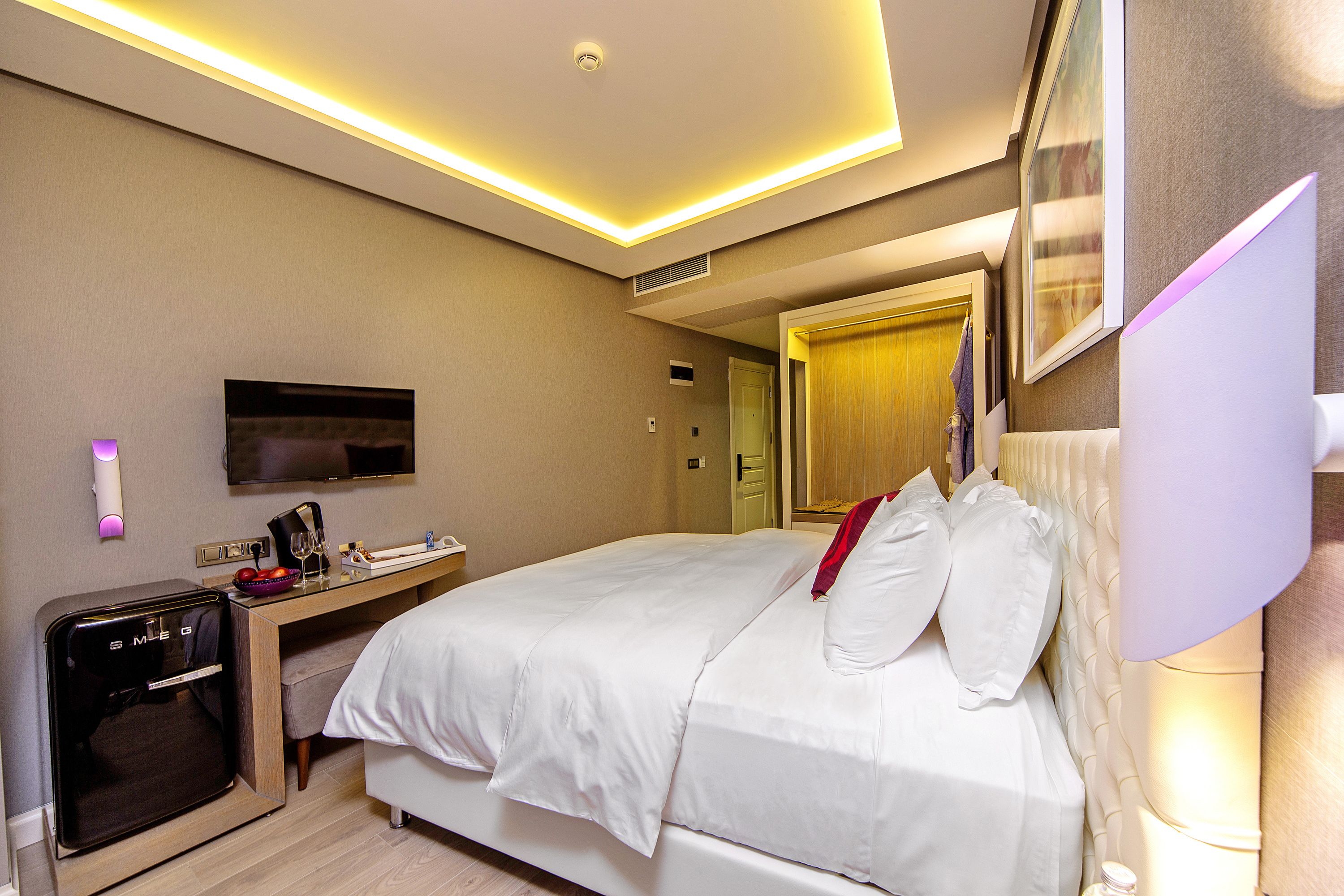 A hotel room with a bed, a desk with a computer, a TV, and a minibar.