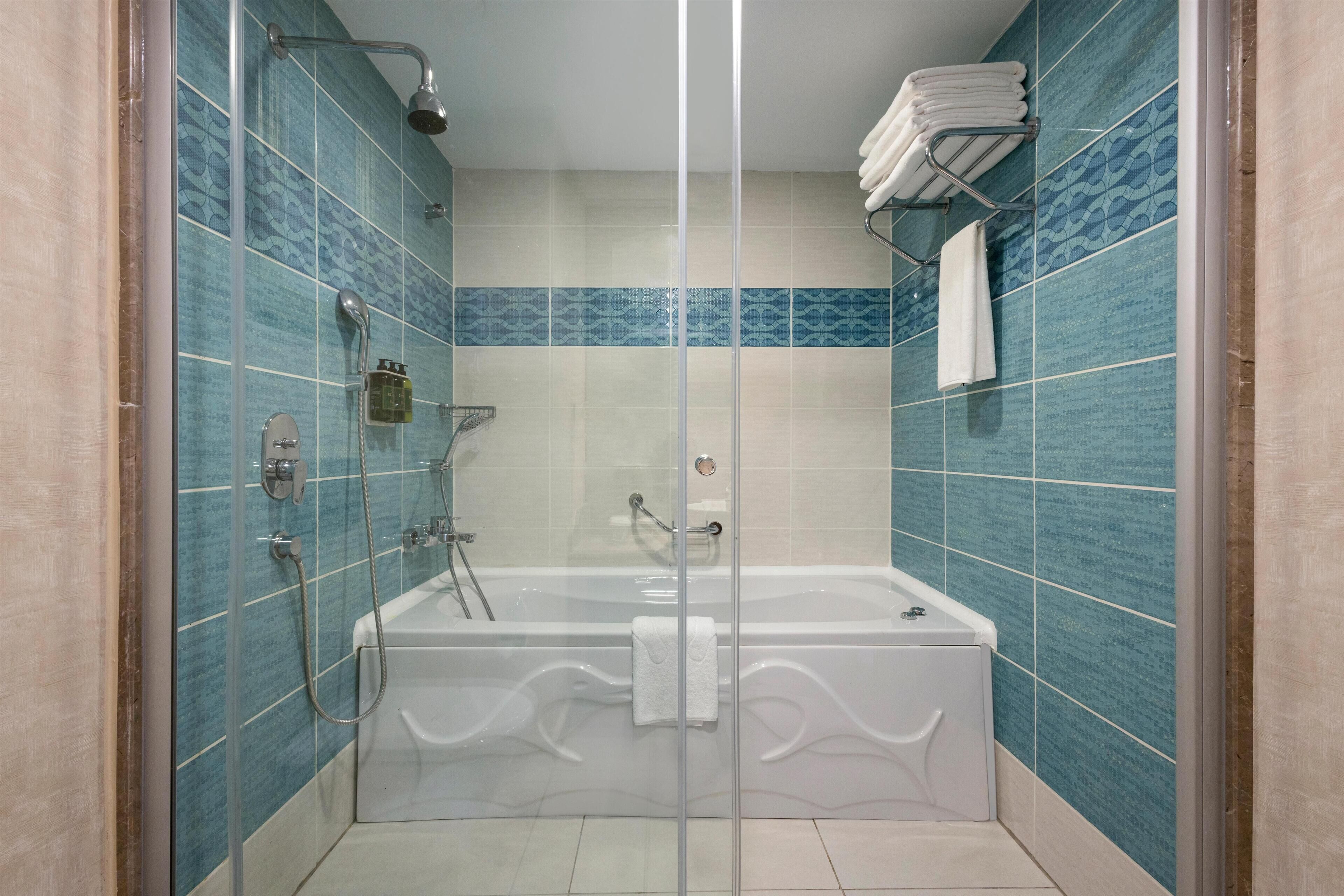 A modern bathroom with a glass-enclosed shower, a freestanding bathtub, and blue-tiled walls.