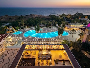 A resort with a large swimming pool, sun loungers, and a view of the ocean.