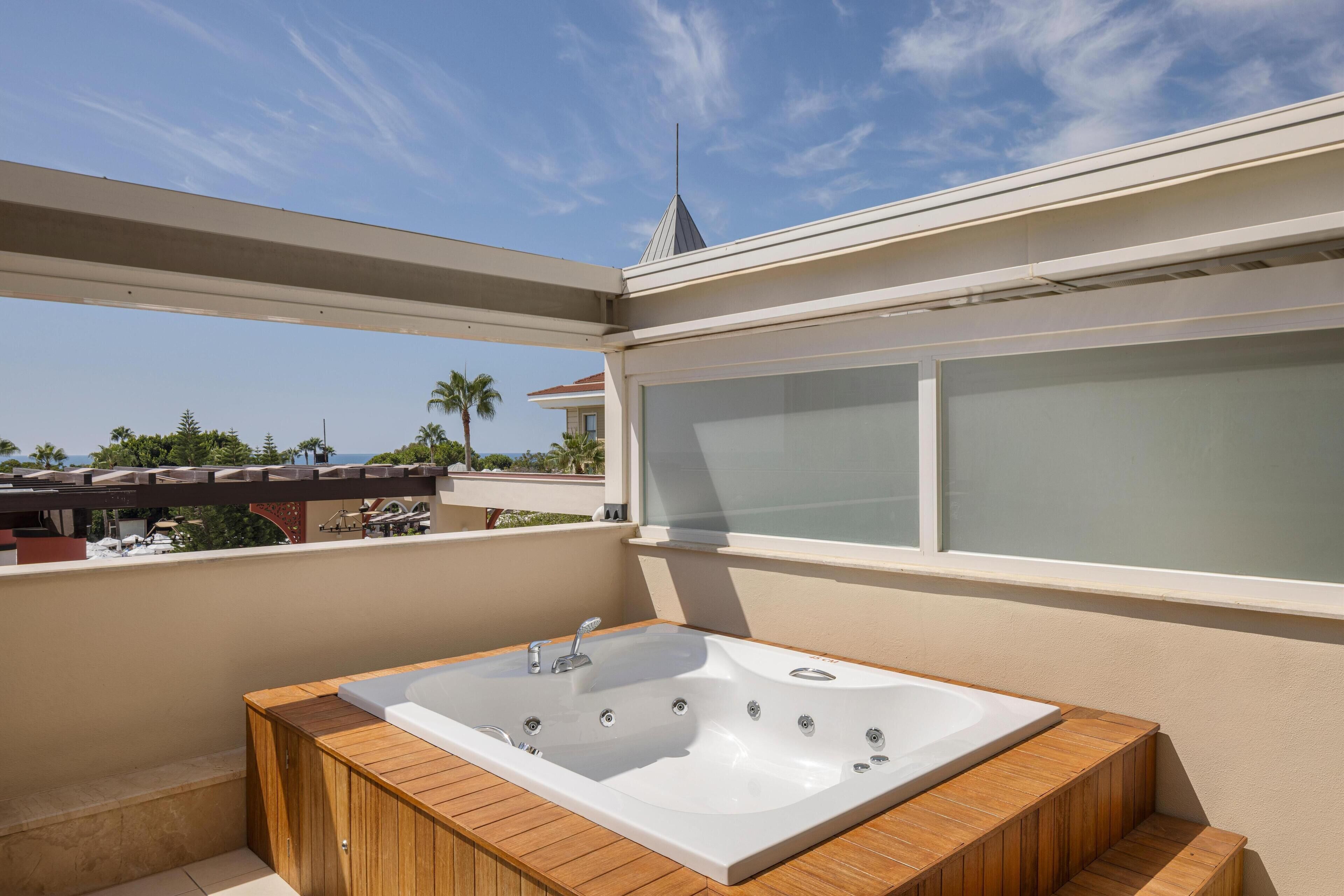 A modern outdoor jacuzzi with a wooden deck, a large window, and a view of the surrounding area.