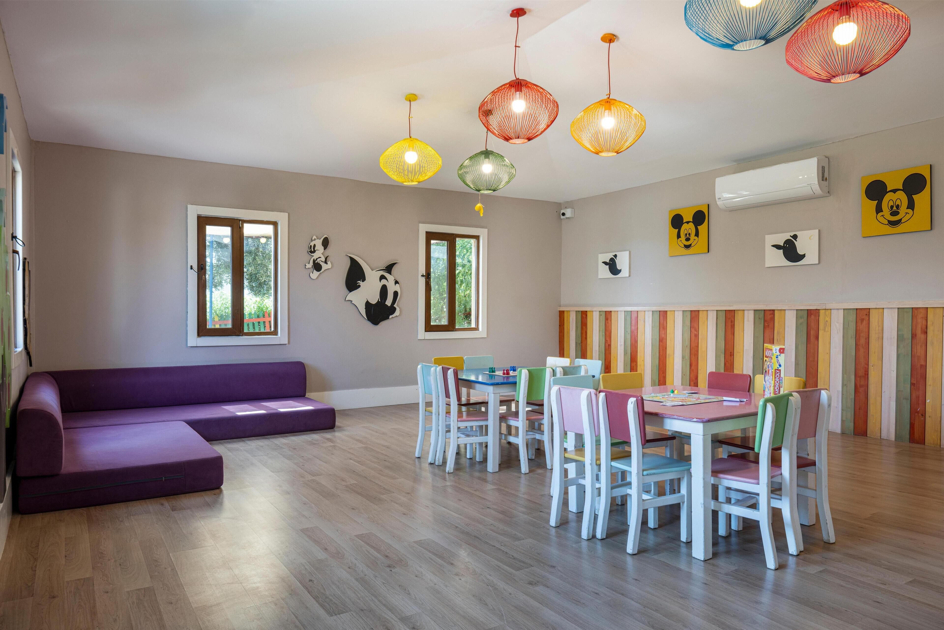 Une salle de jeux pour enfants avec un canapé violet, des chaises colorées, une table et un mur à rayures.