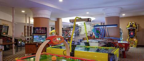 A brightly lit indoor arcade with various gaming machines, including a pool table and claw machines.
