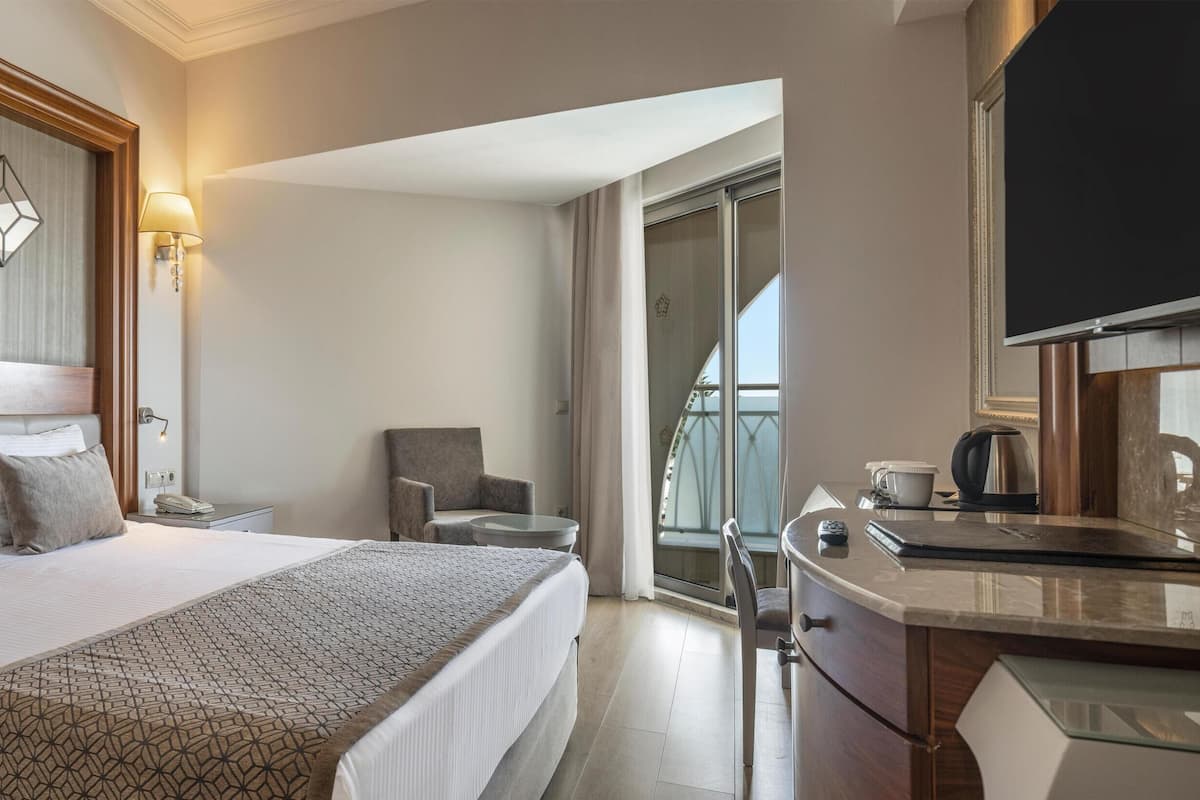 Habitación de hotel con cama, mesita de noche, lámpara, silla y una pequeña zona de kitchenette.