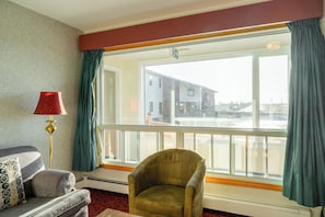 A room with a sofa, armchair, and a large window with curtains.