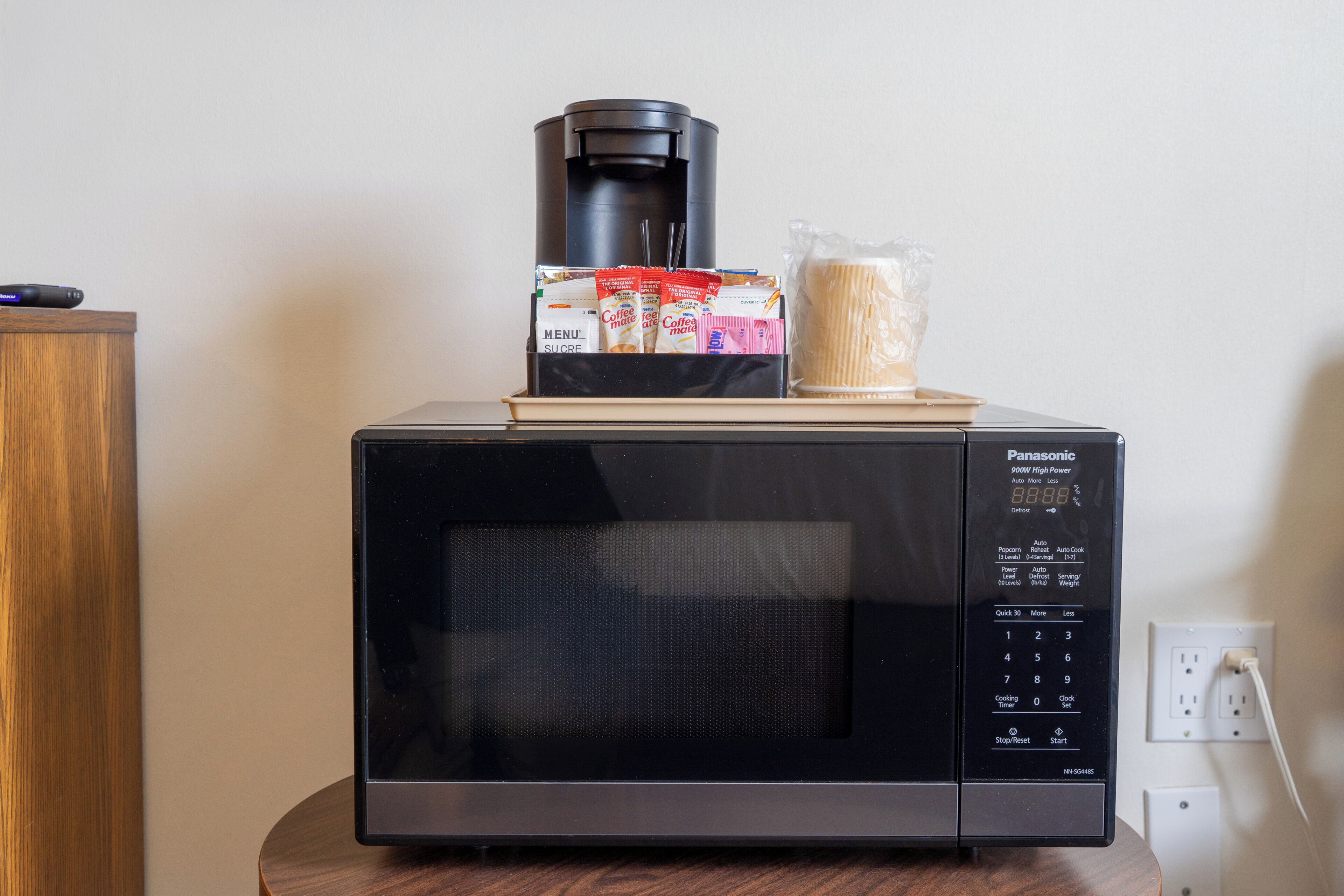 A Panasonic microwave with a coffee maker, a packet of sugar, and a plastic bag of pasta on top.