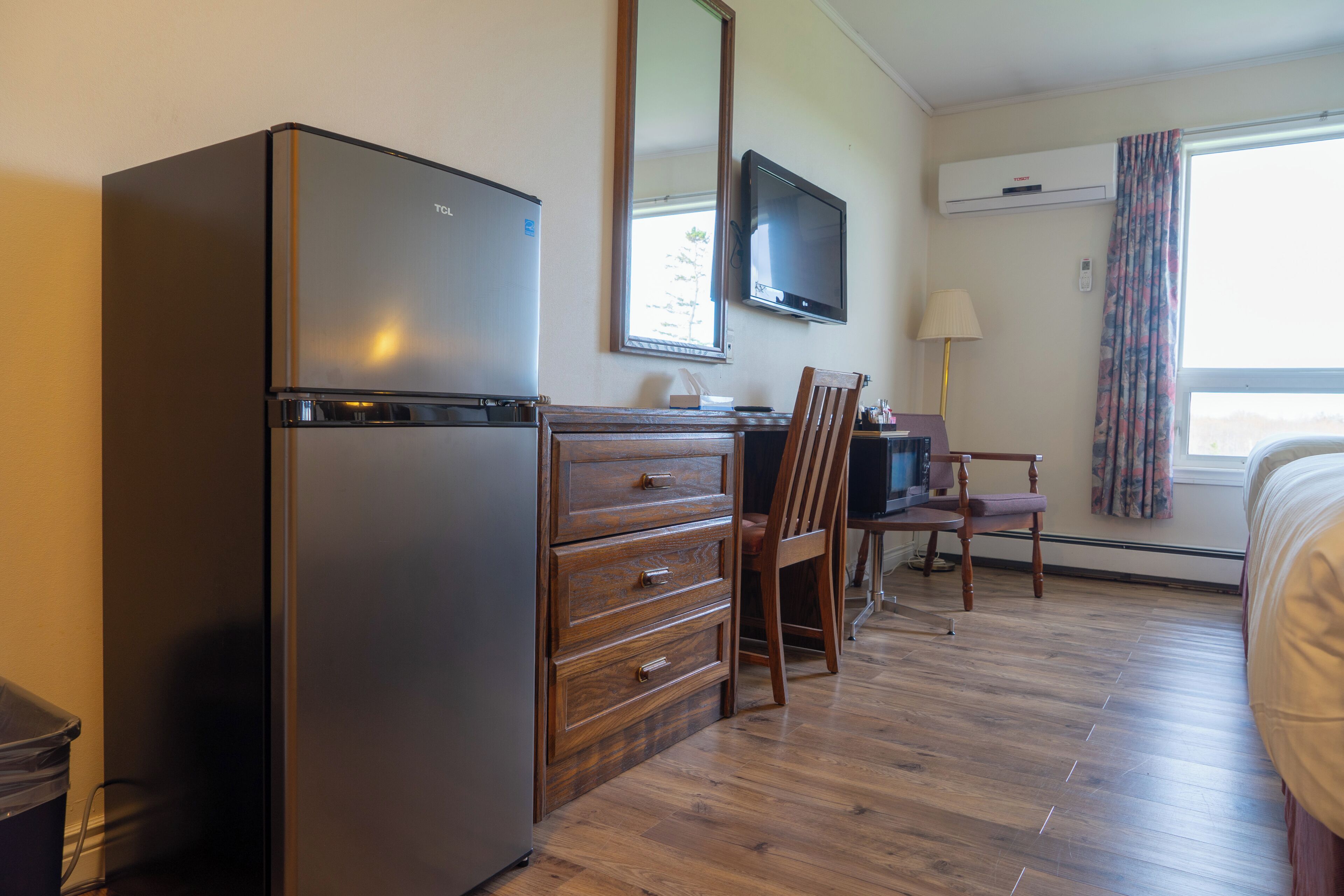 Una habitación con refrigerador, televisión, escritorio con cajones, una silla y una cama.