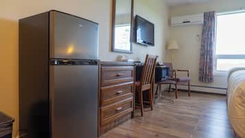 Una habitación con refrigerador, televisión, escritorio con cajones, una silla y una cama.