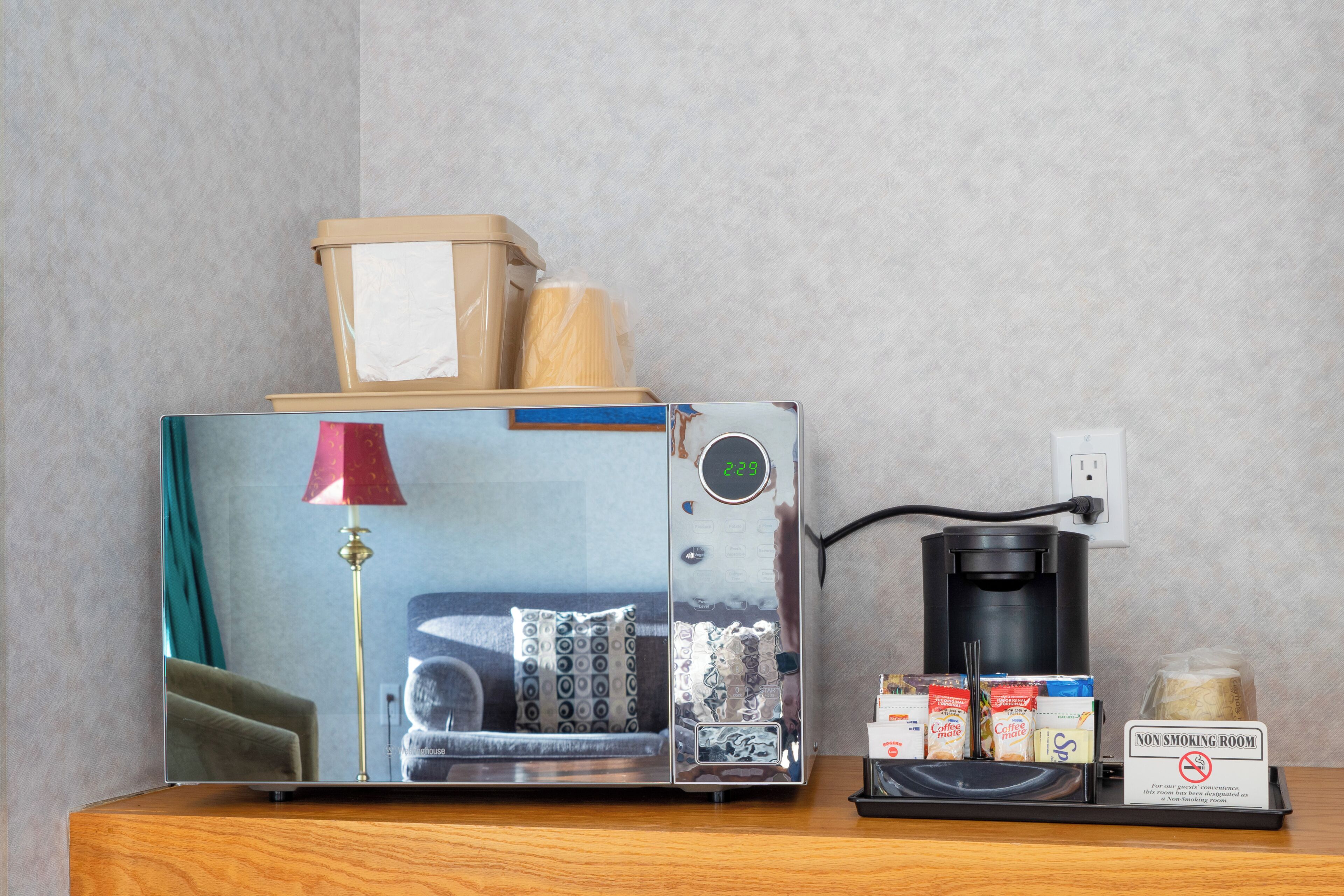 Une machine à café avec minuterie, un panneau «interdiction de fumer», un plateau contenant des dosettes de café et une boîte à pain.
