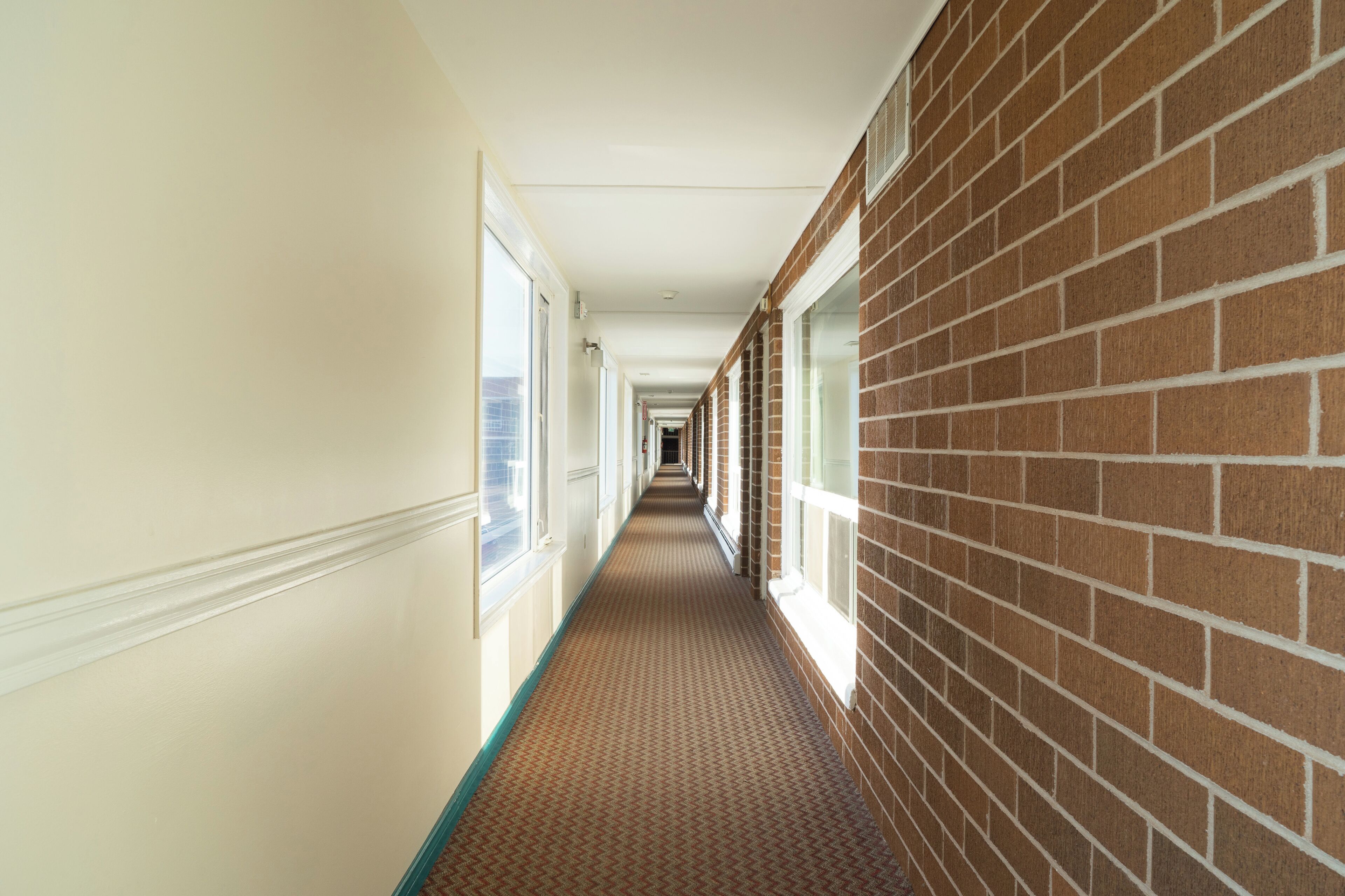 A corridor with a patterned carpet, white walls, and a brick wall on one side.