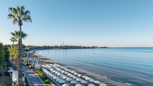 Une promenade en bord de mer bordée de rangées de chaises longues et de parasols, de palmiers, et offrant une vue dégagée sur la mer.