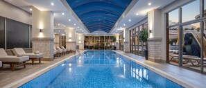 En stor indendørs swimmingpool med liggestole og en glasvæg, der giver udsigt ud