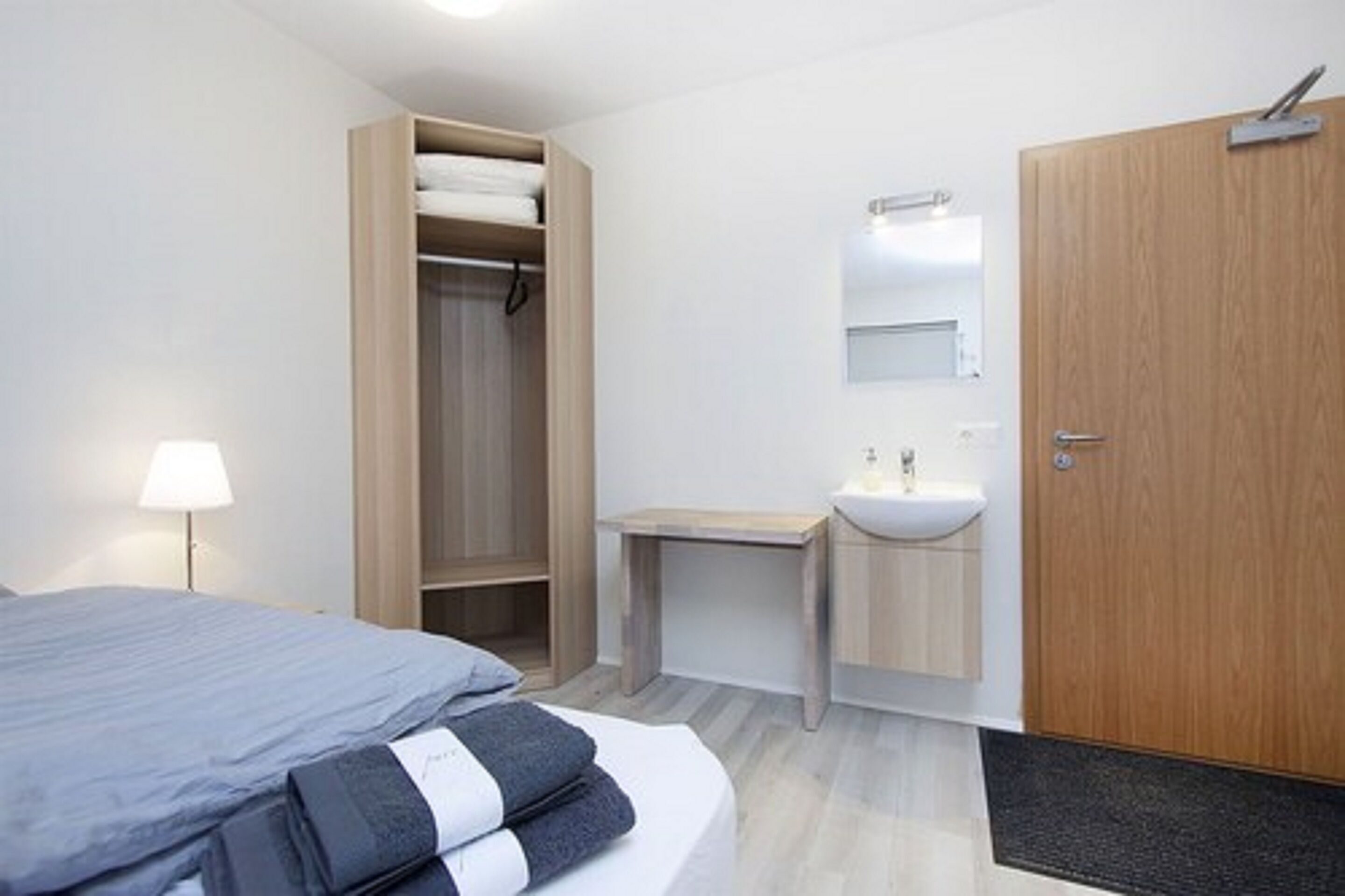 Une chambre d’hôtel moderne équipée d’un lit, d’une armoire en bois, d’une table de chevet, d’un lavabo et d’un miroir.