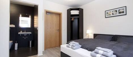 A modern hotel room with a bed, a bedside table, a small bathroom with a sink, and a closet.