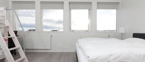 A modern bedroom with a bed, a ladder, and three windows.