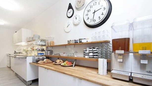 A kitchen with white cabinets, a wooden countertop, and various kitchen appliances. There are clocks on the wall and a coffee machine on the counter.