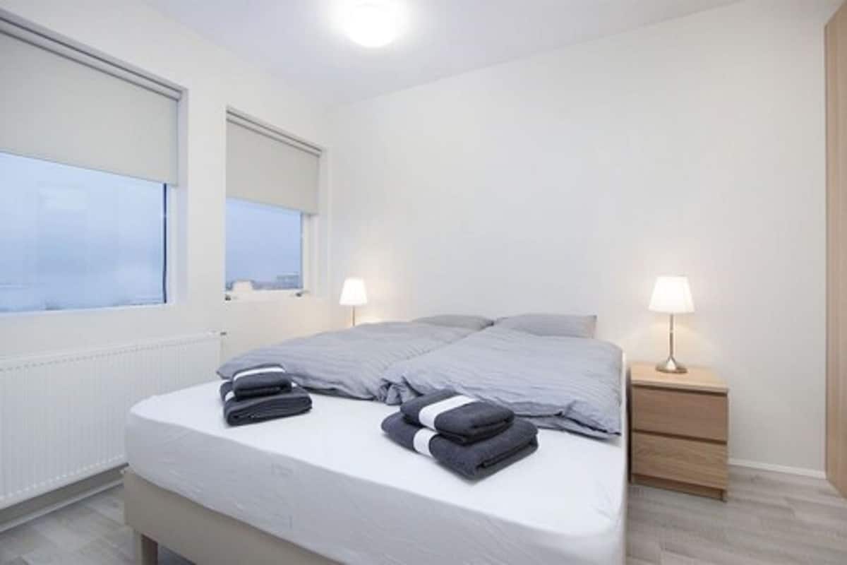 A modern bedroom with a bed, two bedside tables, and a window with blinds.