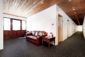 A hallway with a wooden ceiling, a brown leather sofa, a small table, and a door with a sign. - Kef Guesthouse by Keflavík airport (Reykjanesbær)