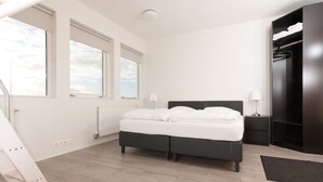 A bedroom with a bed, two bedside tables, a wardrobe, and large windows.