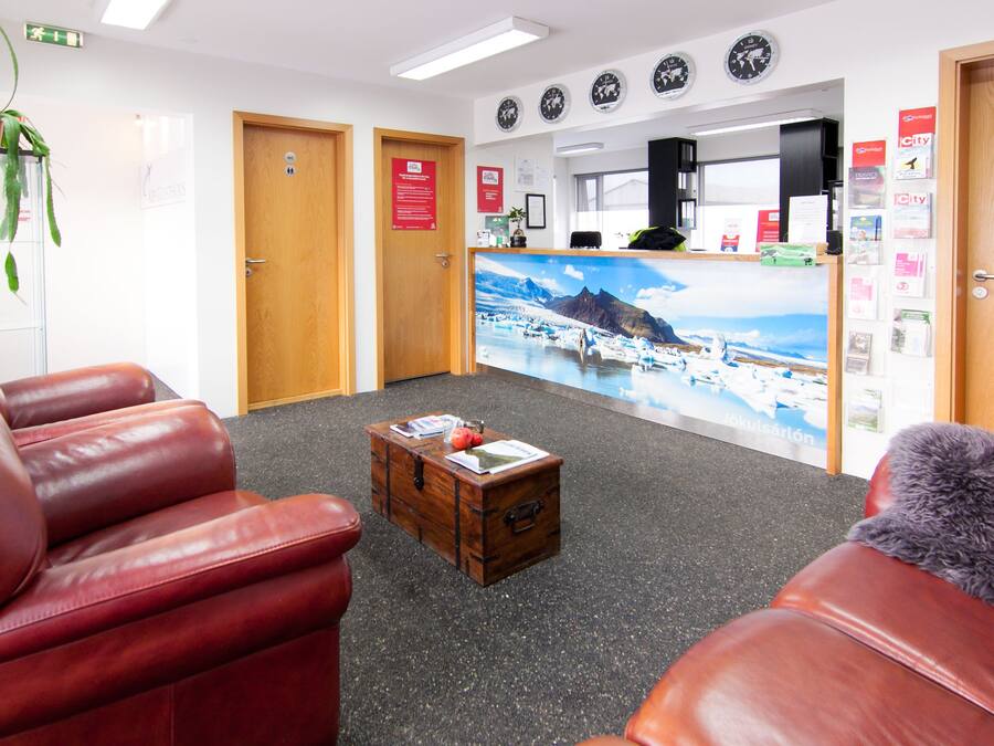 A reception area with a wooden desk, a large wall mural, and red leather seating.