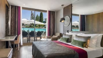 Une chambre d’hôtel moderne avec un grand lit, un bureau et une vue sur l’espace extérieur abritant une piscine.