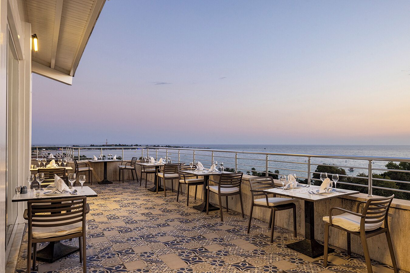 An outdoor dining area with tables and chairs, overlooking a body of water.
