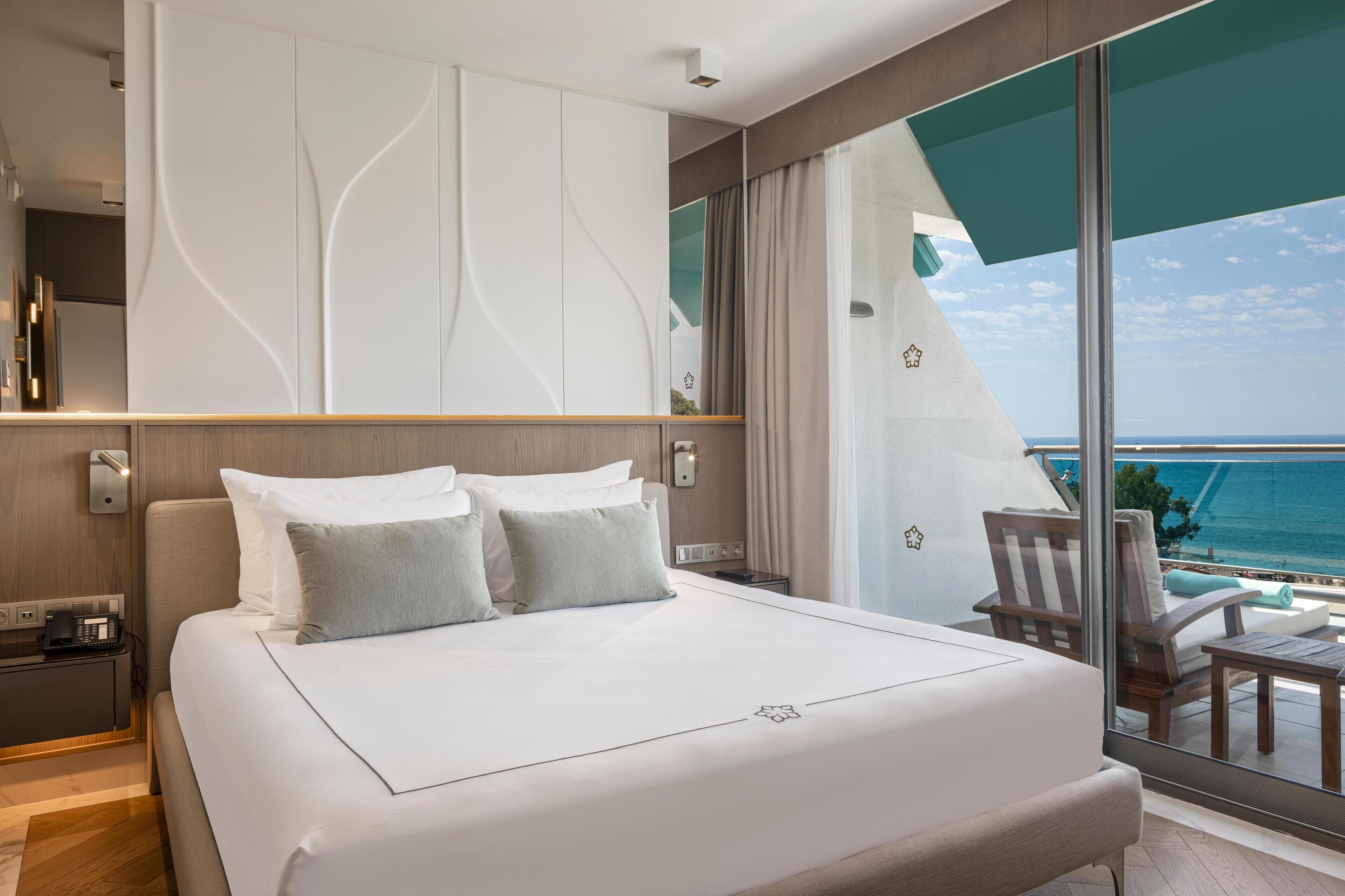 A modern hotel room with a large bed, a balcony with a view of the ocean, and a sleek, contemporary design.