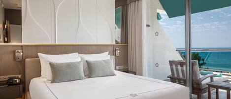 A modern hotel room with a large bed, a balcony with a view of the ocean, and a sleek, contemporary design.