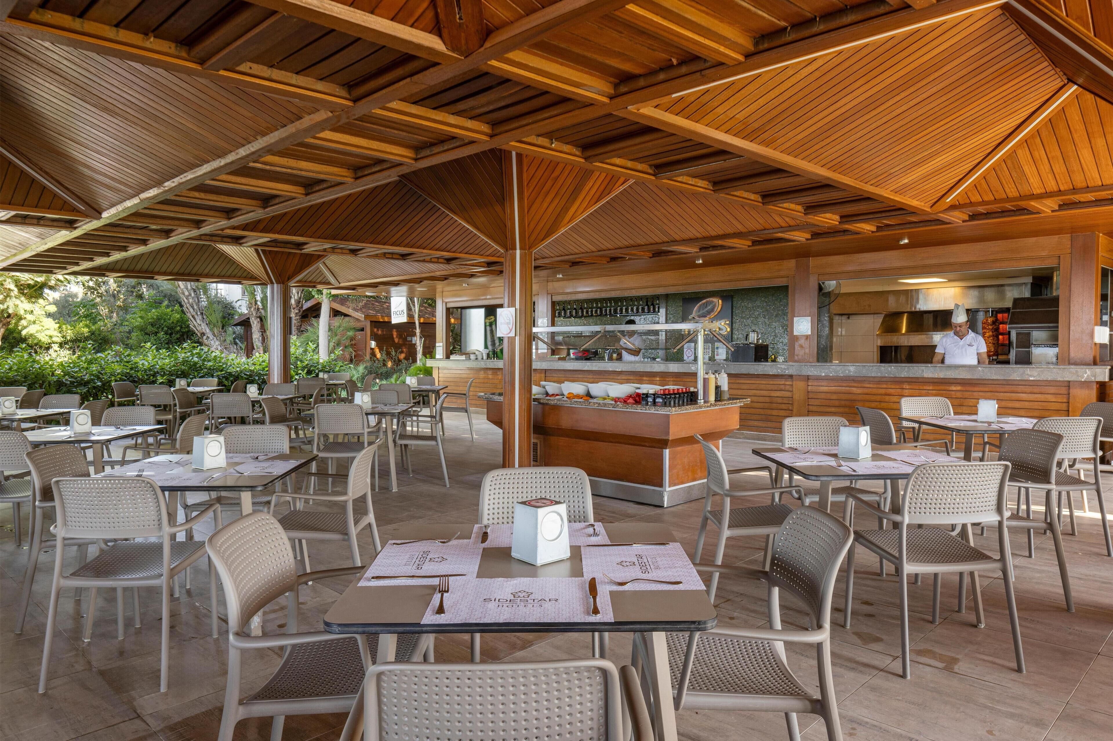 An outdoor dining area with tables and chairs, a bar, and a chef in the background.