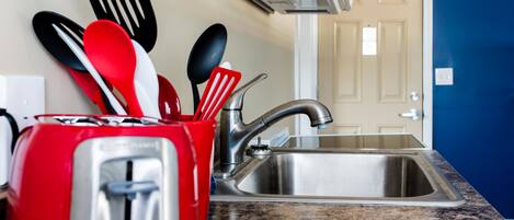 A kitchen with a stainless steel sink, a red toaster, and various kitchen utensils.