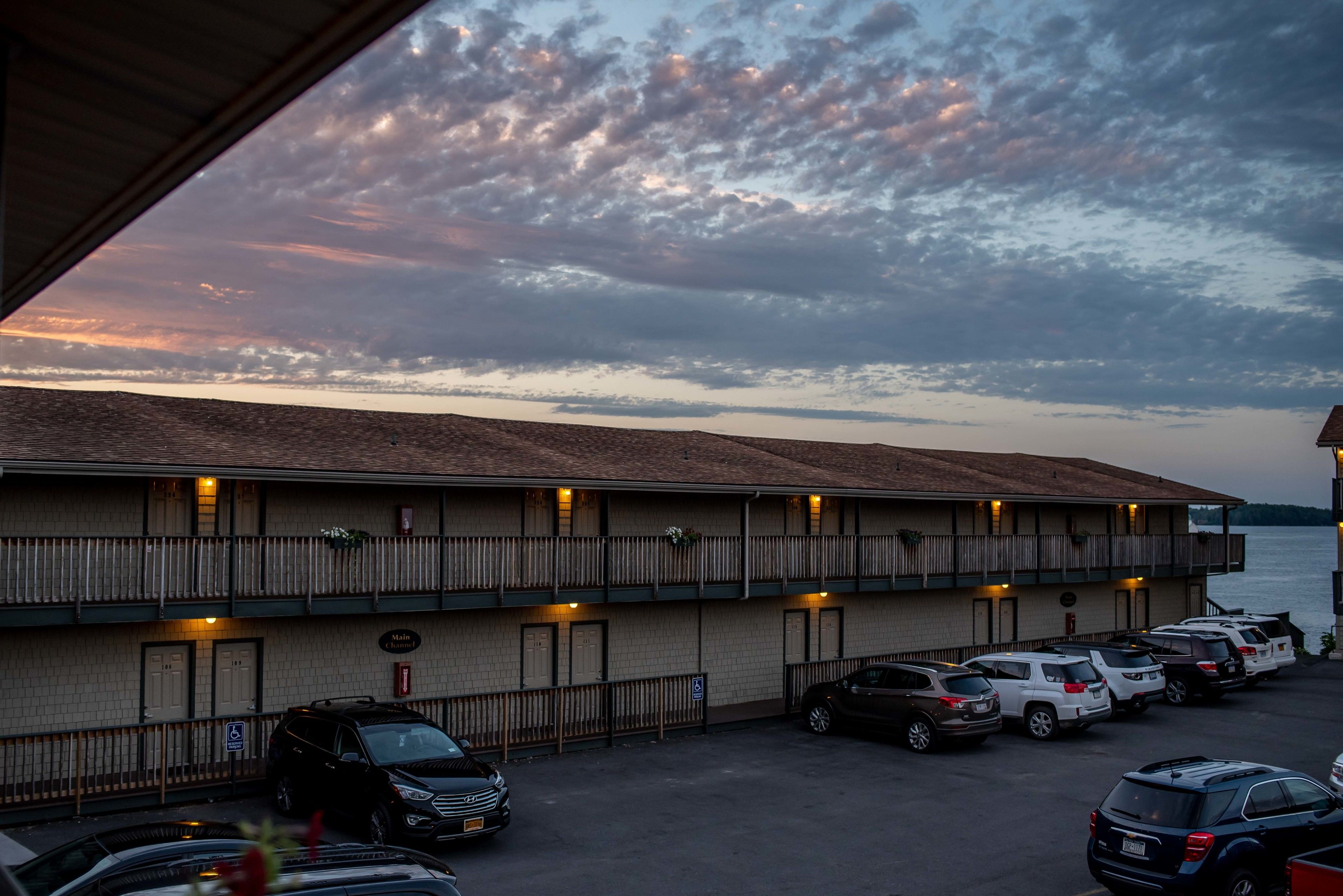 A motel with a parking lot, a view of the water, and a sunset sky.