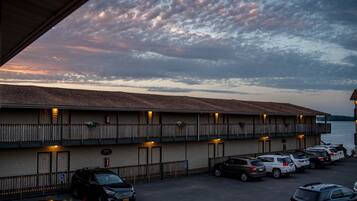 A motel with a parking lot, a view of the water, and a sunset sky.