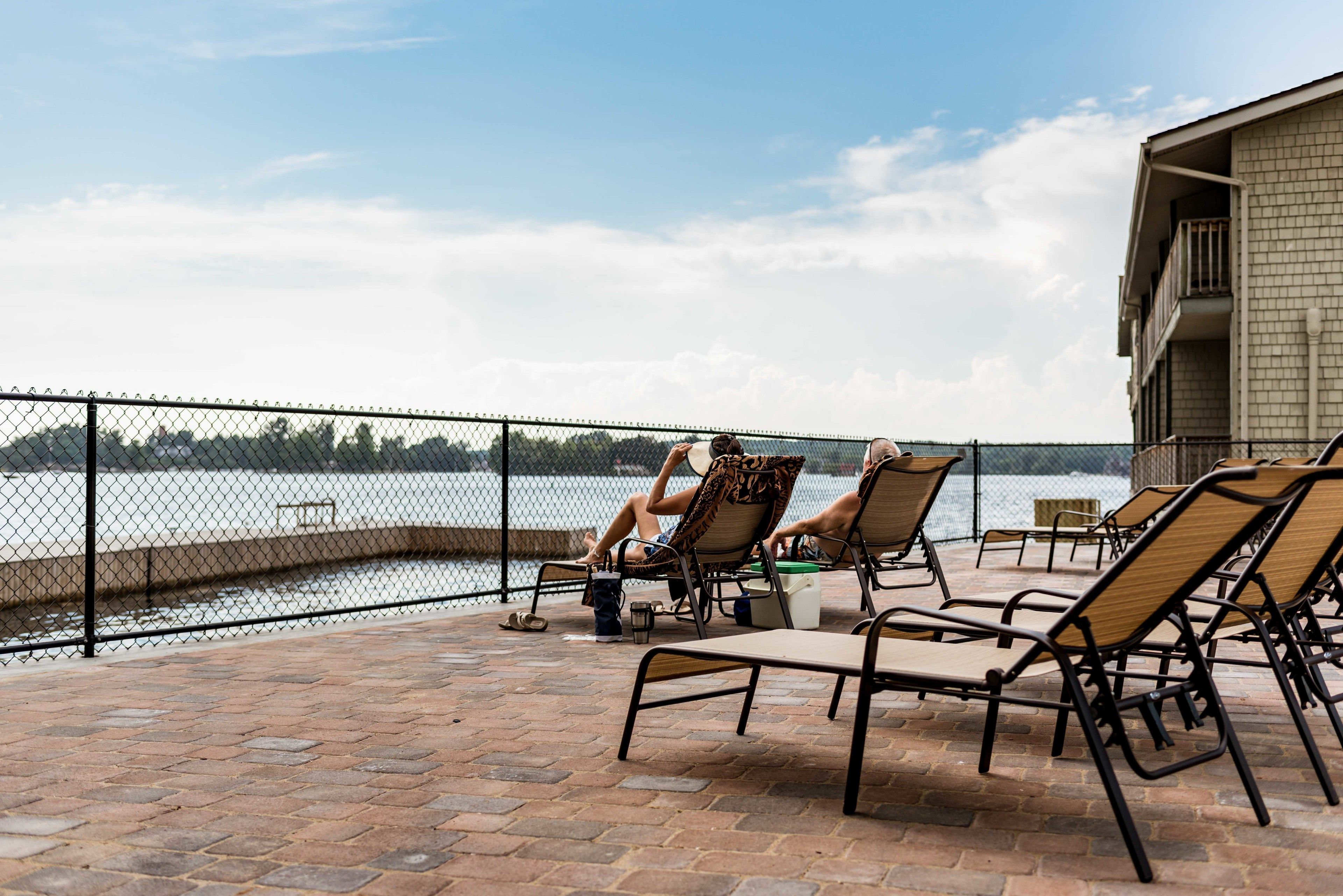 A patio with lounge chairs overlooking a body of water, enclosed by a fence.