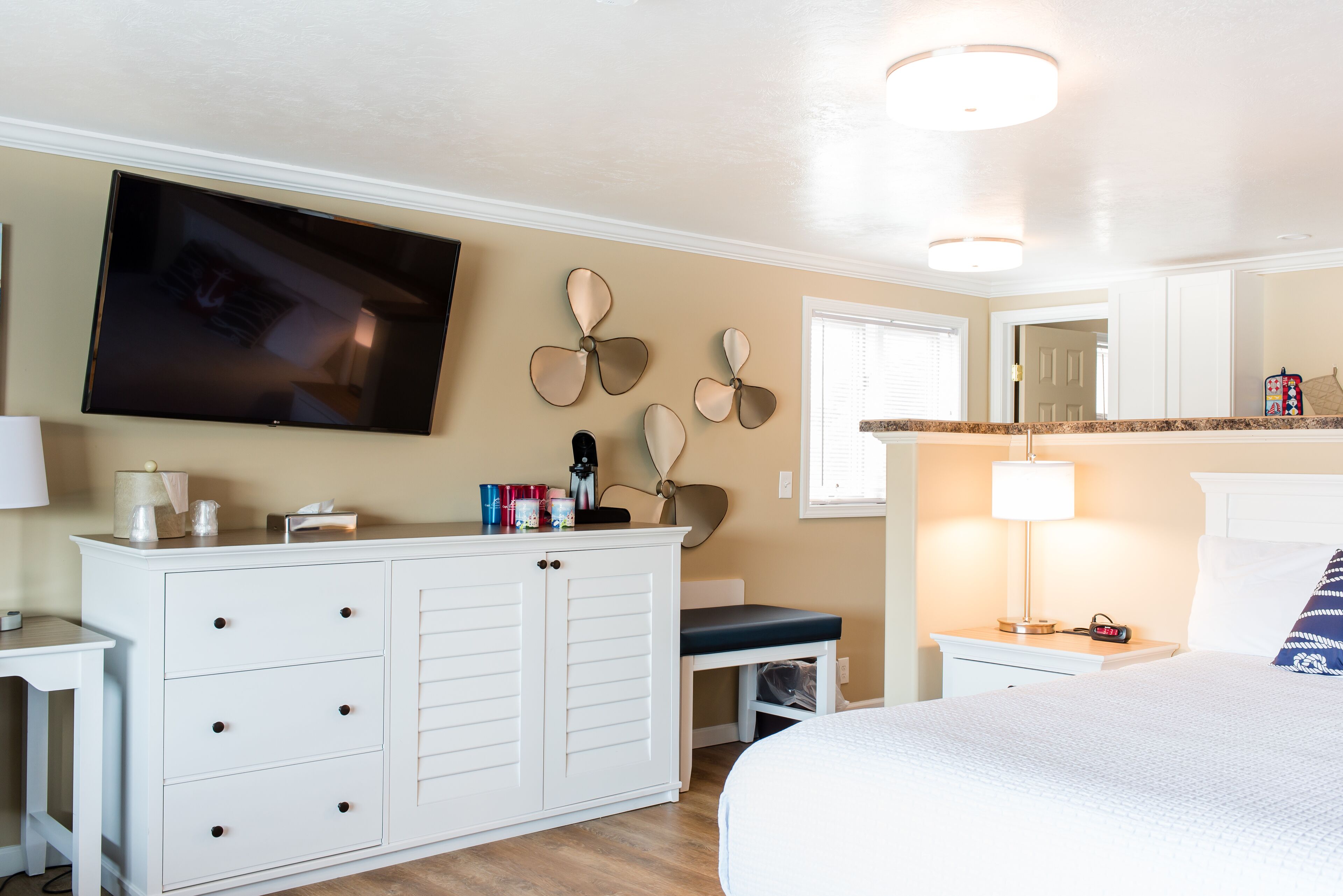 A bedroom with a bed, a dresser, a TV mounted on the wall, and a ceiling fan.
