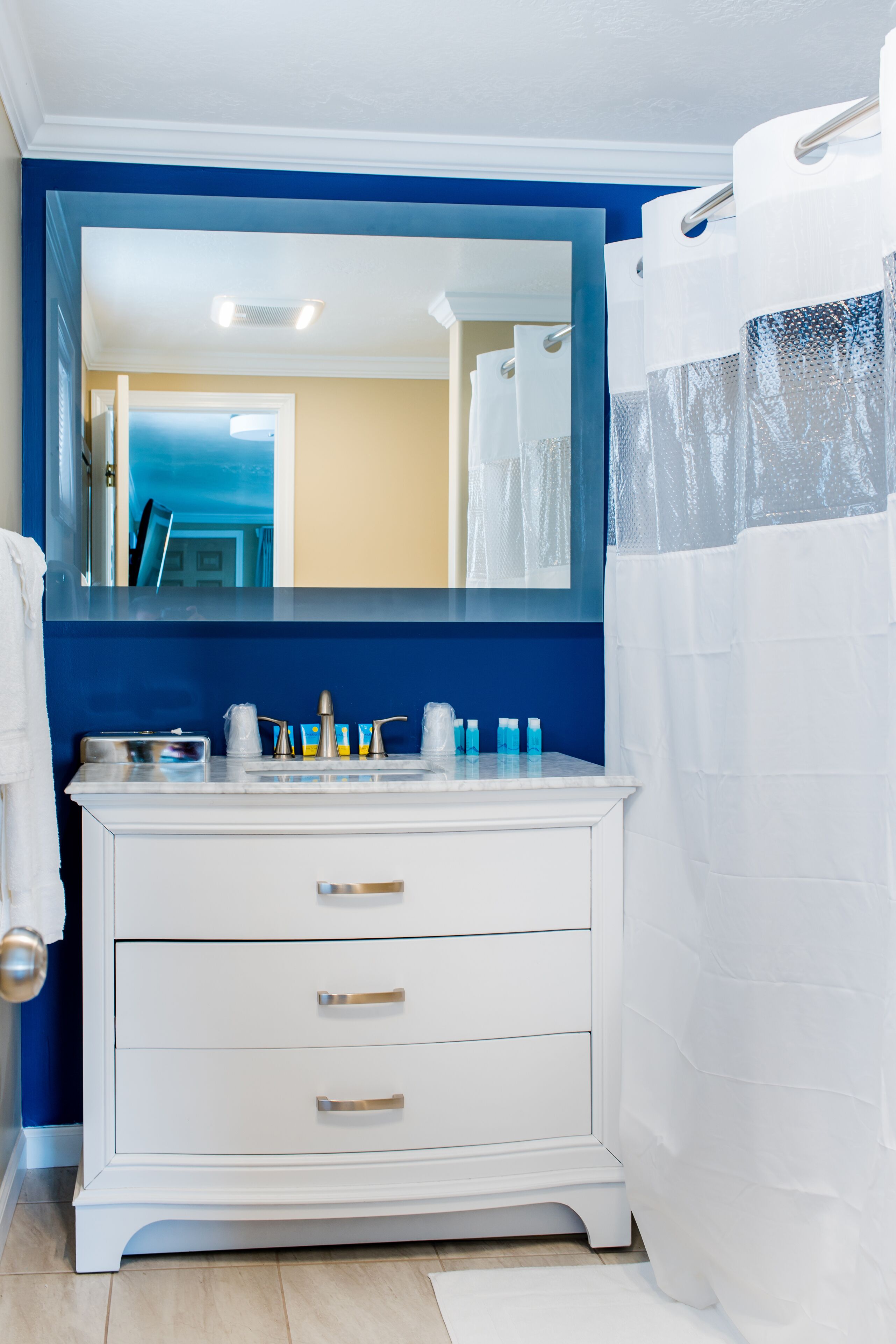 Ein Badezimmer mit weißem Waschtisch, blauer Akzentwand und weißer Duschvorhang.