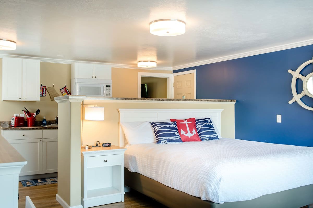 A bedroom with a bed, nightstands, a dresser, and a microwave in the kitchen area.
