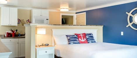 A bedroom with a bed, nightstands, a dresser, and a microwave in the kitchen area.