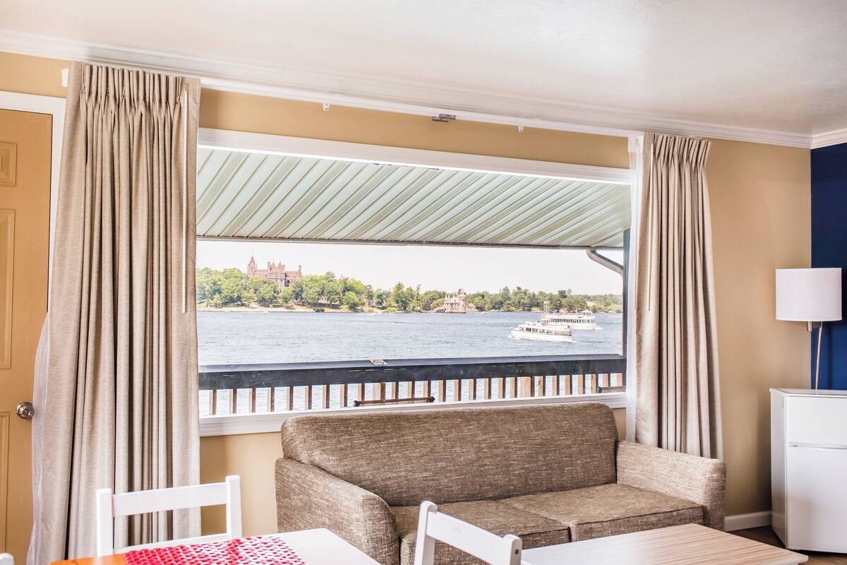 A room with a view of a body of water, a sofa, a table, and a lamp.