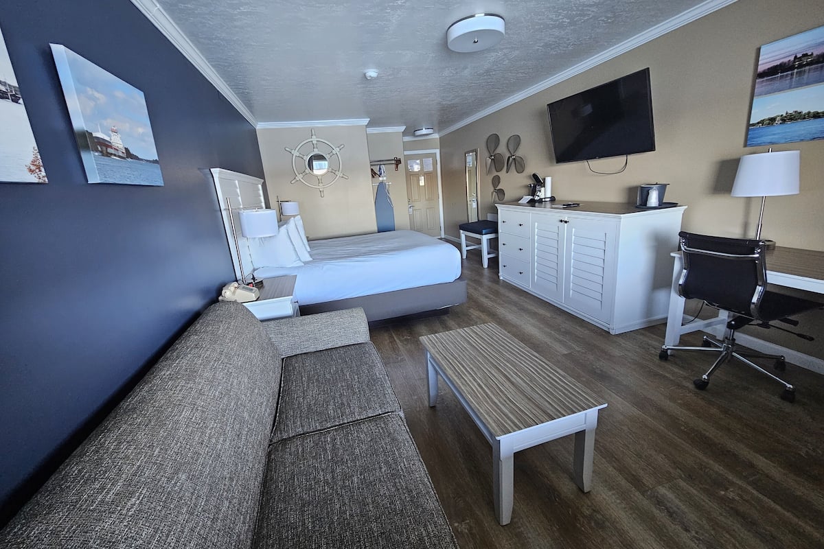 A hotel room with a bed, a desk, a chair, a TV, and artwork on the walls.