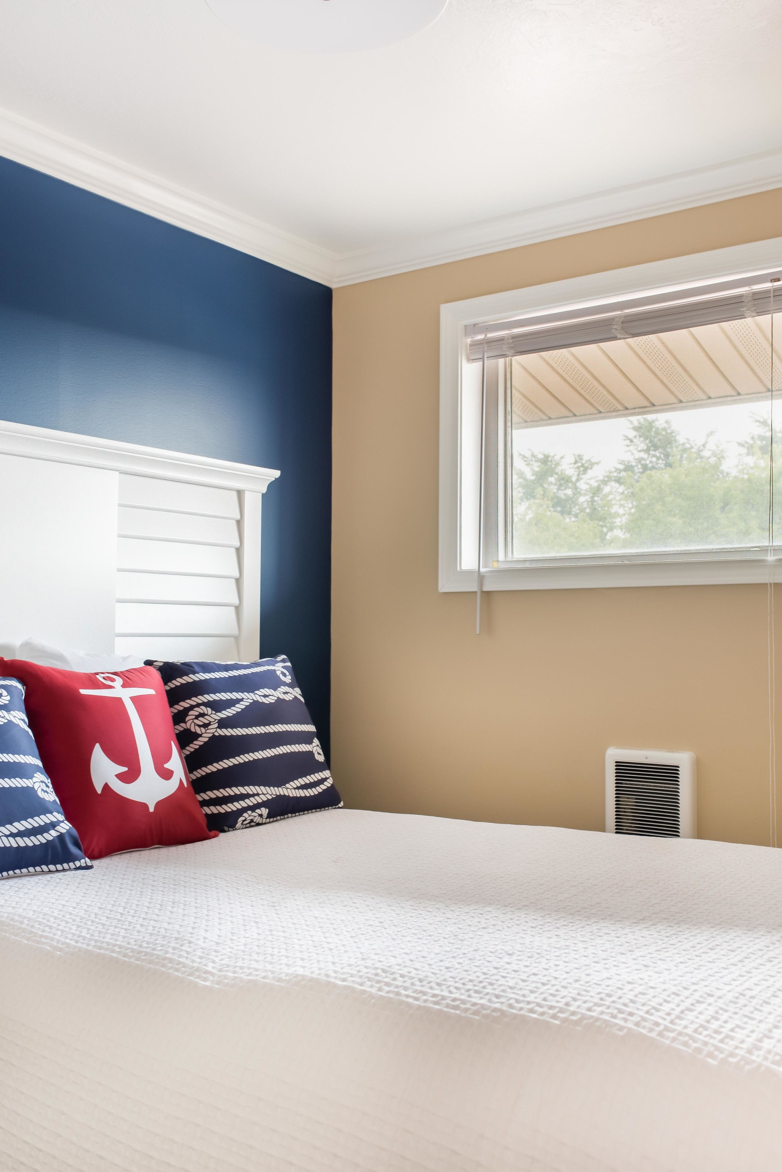A bedroom with a bed, a window with blinds, a white ceiling, and a wall painted in two colors.