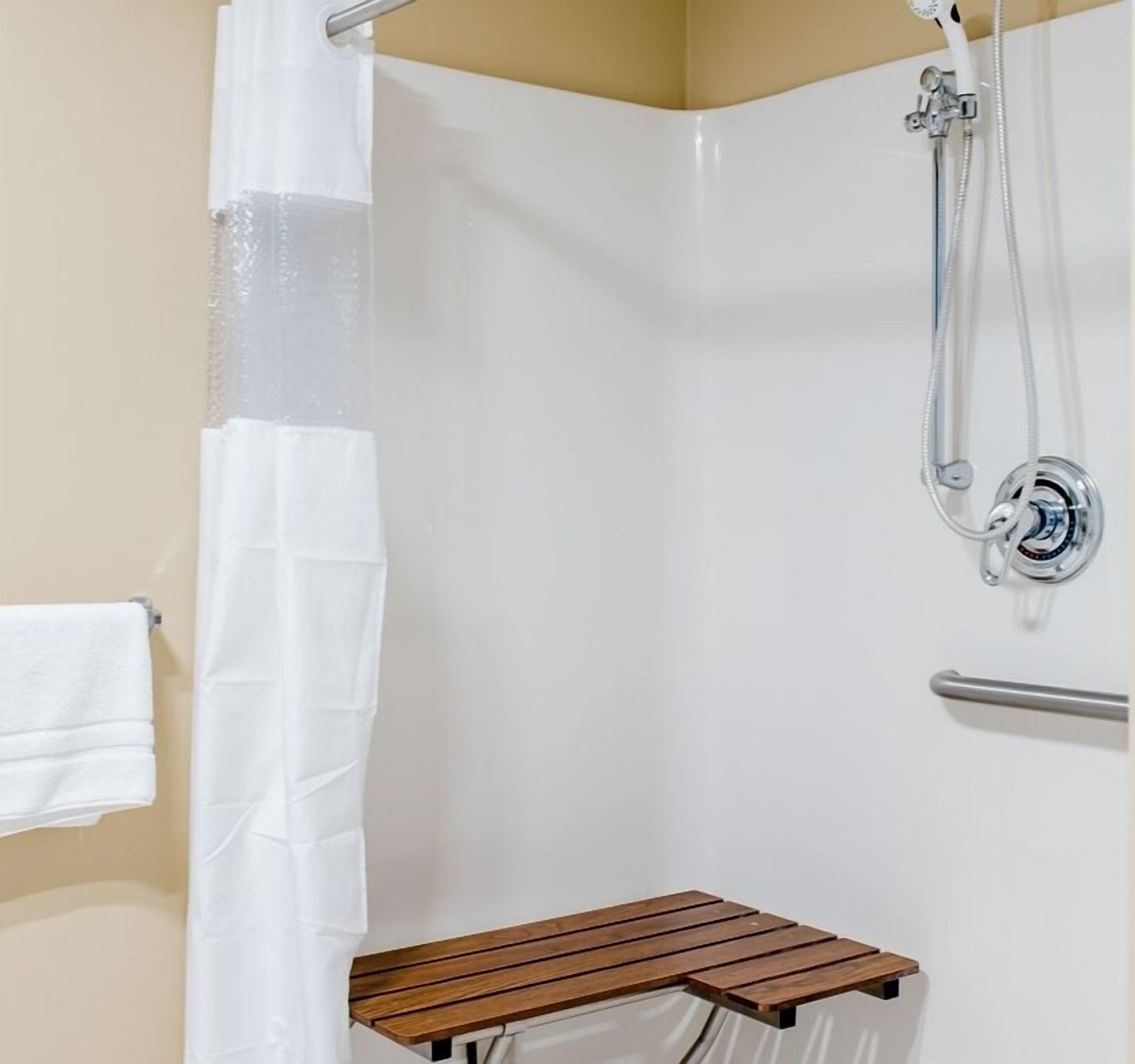A shower area with a white shower curtain, a handheld showerhead, and a wooden bench.