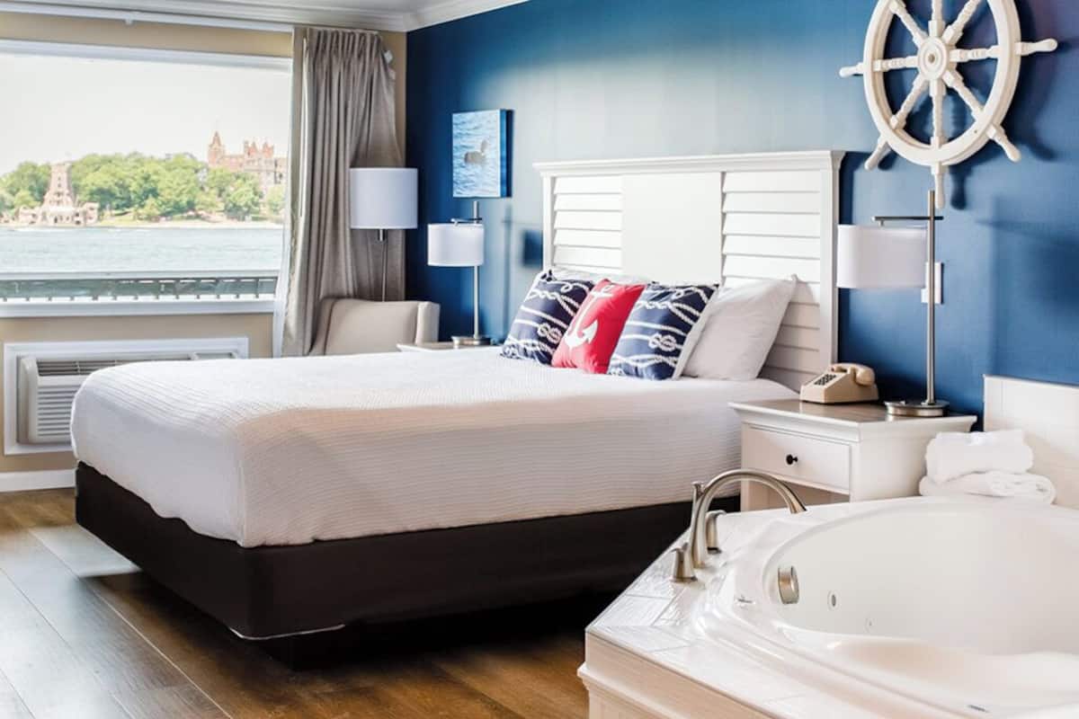 A hotel room with a large bed, a white bathtub, and a view of a castle through the window.