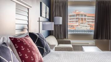 Habitación de hotel con cama, una silla, un escritorio y ventana con vista a un edificio.