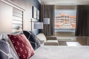 A hotel room with a bed, a chair, a desk, and a window with a view of a building.
